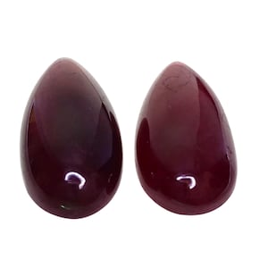 May include: Two teardrop-shaped cabochons with a deep, dark red color and a smooth, polished surface. These gemstones feature a rounded top and a flat base, reflecting light with a glossy sheen across their opaque, solid red surfaces.