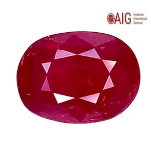 May include: A vibrant oval-cut red ruby gemstone featuring a faceted surface with a star-like pattern. The gemstone is displayed alongside the logo and text for the American International GemLab in the upper right corner.