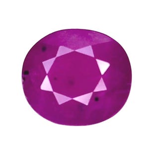May include: A round, vibrant magenta gemstone featuring a faceted surface with a central star-shaped pattern. The stone displays a deep pinkish-purple hue with visible internal inclusions and sharp geometric light reflections across its top.