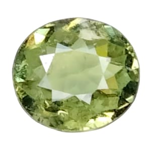 May include: A round, faceted gemstone with a pale green hue. The gem has a star-like pattern in the center, with a mix of light and dark green tones throughout. The gemstone is set against a white background.