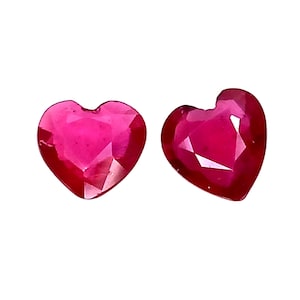 May include: Two loose, heart-shaped faceted gemstones with a deep, vibrant red color. Each stone features a polished surface with multiple triangular facets that reflect light, creating a brilliant, sparkling appearance against a white background.