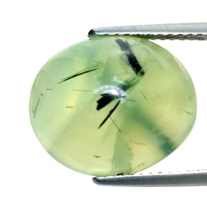 May include: A round, translucent gemstone, held by tweezers. The gem is a pale green color with black inclusions. The stone is smooth and polished, with a slight sheen. The background is white.