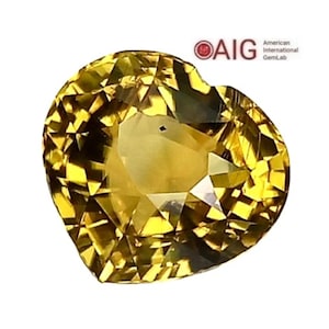 May include: A heart-shaped, faceted gemstone with a brilliant yellow color. The gem has many facets that reflect light, creating a sparkling effect. The image includes the text "AIG American GemLab".