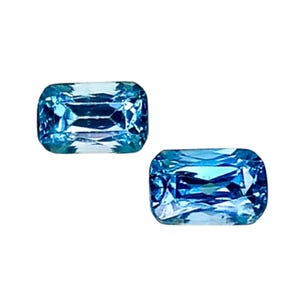 May include: Two rectangular, light blue gemstones with rounded corners are displayed against a white background. The gems have internal facets that reflect light, creating a sparkling effect. These gems are likely for jewelry.