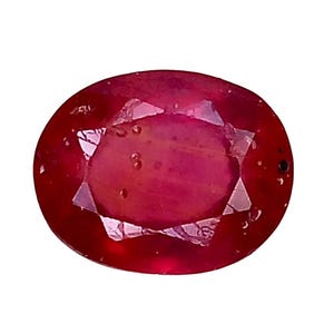 Op de afbeelding: Een ovaal geslepen robijn, diep rood van kleur. De facetten creëren een stervormig patroon in het midden. De edelsteen staat tegen een witte achtergrond. Robijnen worden vaak in sieraden gebruikt.
