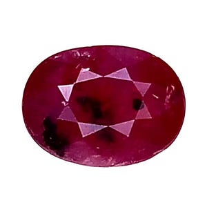 Puede incluir: Gema roja oscura de forma ovalada con un patrón de estrella facetada en el centro. El rubí tiene una superficie pulida y está sobre un fondo blanco. El color de la gema es un rojo intenso y saturado.