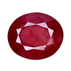 May include: An oval-shaped, faceted gemstone with a deep red color. The stone features a central oval table surrounded by multiple triangular and trapezoidal facets that reflect light, creating a symmetrical pattern across the surface of the gem.