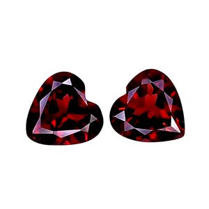 May include: Two loose heart-shaped gemstones with a deep red color and faceted surfaces. These stones exhibit a clear, transparent quality with sharp geometric cuts that reflect light across their polished, symmetrical surfaces.
