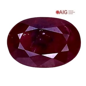 May include: An oval-cut, deep red gemstone with a faceted surface. The stone displays a dark, saturated crimson hue and is accompanied by the AIG American International GemLab logo and text in the upper right corner of the frame.