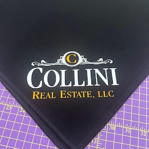 May include: Black fabric with a white embroidered logo that says "Collini Real Estate, LLC" with a gold "C" in a circle.