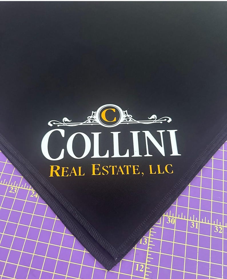 May include: Black fabric with a white embroidered logo that says "Collini Real Estate, LLC" with a gold "C" in a circle.