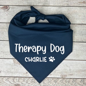 Może przedstawiać: Niebieska bandana dla psa z białym napisem "Therapy Dog CHARLIE" i odciskiem łapy.