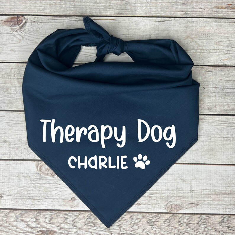 Może przedstawiać: Niebieska bandana dla psa z białym napisem "Therapy Dog CHARLIE" i odciskiem łapy.