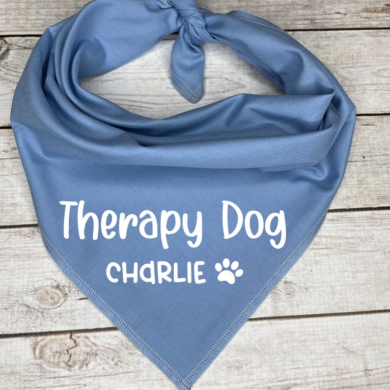 Może przedstawiać: Jasnoniebieska bandana dla psa z białym napisem "Therapy Dog Charlie" i odciskiem łapy.