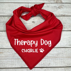 Może przedstawiać: Czerwona bandana z białym tekstem, kt&oacute;ry brzmi "Therapy Dog CHARLIE" z odciskiem łapy.