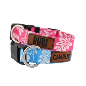 May include: Two dog collars with tropical floral patterns. The pink collar has the name "Rubi" on it and the blue collar has the name "Charlie" on it.