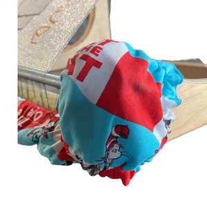 May include: A wooden box with a sparkly, silver-colored lid and a Dr. Seuss-themed scrunchie. The scrunchie features a red, white, and blue pattern with the Cat in the Hat character and text.
