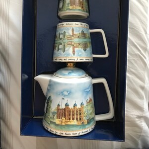 May include: A white ceramic tea set featuring a London theme. The teapot, creamer and sugar bowl are decorated with images of famous London landmarks, including the Tower of London, Big Ben and the Houses of Parliament. The set is packaged in a blue box.