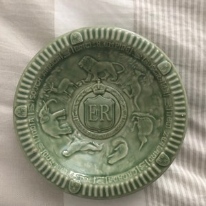May include: A pale green ceramic plate with a raised relief design. The plate features a central crest with the initials "ER" and is surrounded by images of animals and text that reads "British Empire".