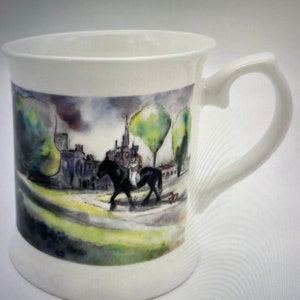 Könnte beinhalten: Weiße Keramiktasse mit einer Aquarell-Illustration eines schwarzen Pferdes und Reiters in einer Parklandschaft. Die Illustration zeigt Bäume, Gebäude und einen Weg.