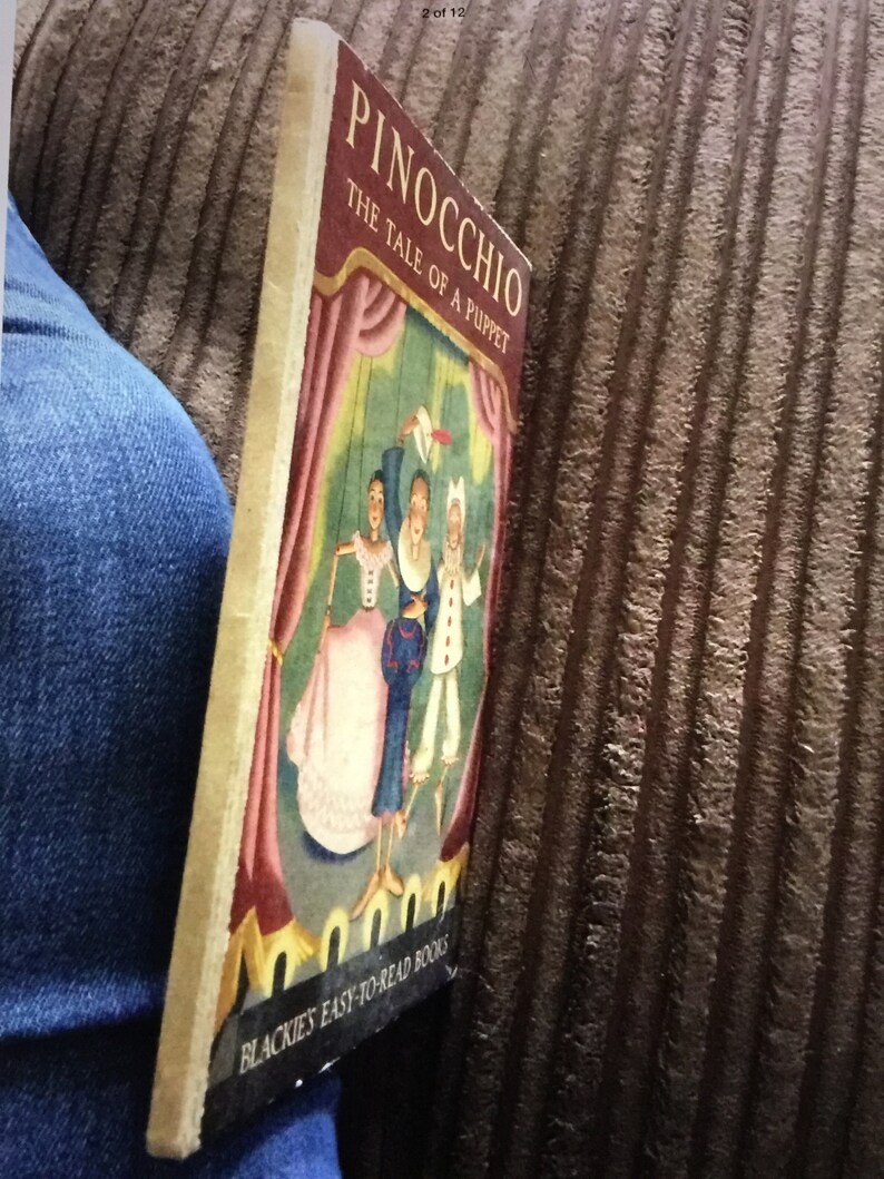 May include: A vintage copy of "Pinocchio: The Tale of a Puppet" by Blackie's Easy-to-Read Books. The cover features a colorful illustration of the puppet show with characters in costume. The book is held against a blue denim background.
