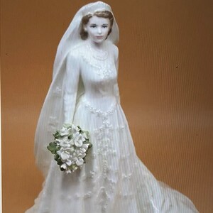 May include: A white porcelain figurine of a bride wearing a white gown with a veil and holding a bouquet of white flowers.