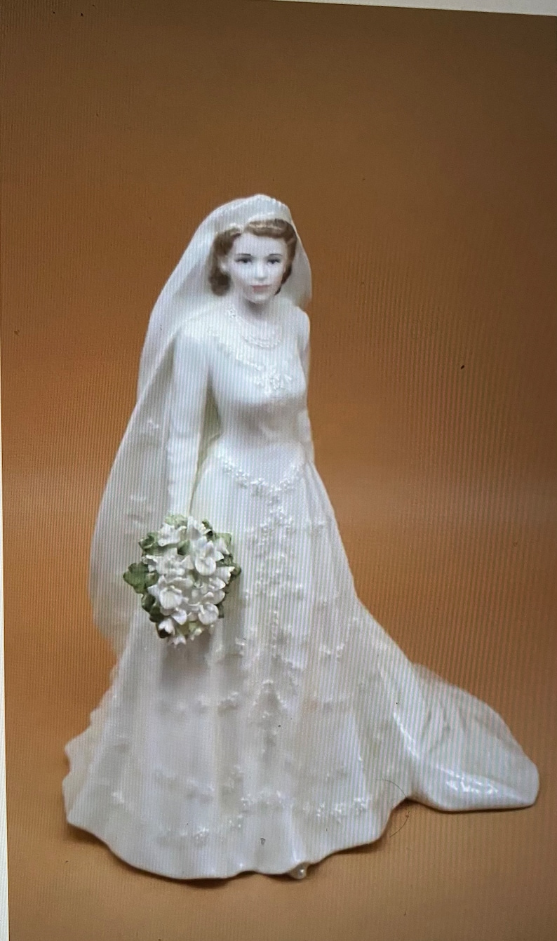 May include: A white porcelain figurine of a bride wearing a white gown with a veil and holding a bouquet of white flowers.