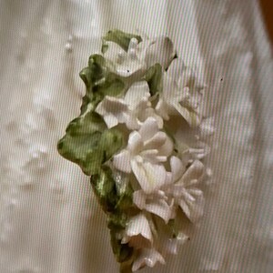 May include: A close-up of a white porcelain flower with green leaves. The flower is delicate and intricate, with a realistic appearance.