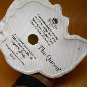 May include: White porcelain figurine of Queen Elizabeth II, commemorating her marriage to the Duke of Edinburgh on November 20, 1947. The figurine is part of a limited edition of 7,500 pieces, numbered 616. The base of the figurine is inscribed with the text 'The Queen' and 'Sculpted by Brandby'.
