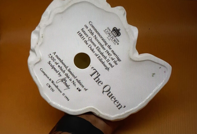 May include: White porcelain figurine of Queen Elizabeth II, commemorating her marriage to the Duke of Edinburgh on November 20, 1947. The figurine is part of a limited edition of 7,500 pieces, numbered 616. The base of the figurine is inscribed with the text 'The Queen' and 'Sculpted by Brandby'.