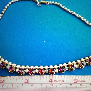May include: A gold chain necklace with a double row of clear and red rhinestones. The necklace is 15 inches long and is measured with a ruler.