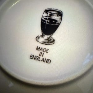 May include: A white ceramic plate with a black illustration of a glass of dark liquid. The words "MADE IN ENGLAND" are printed below the illustration.