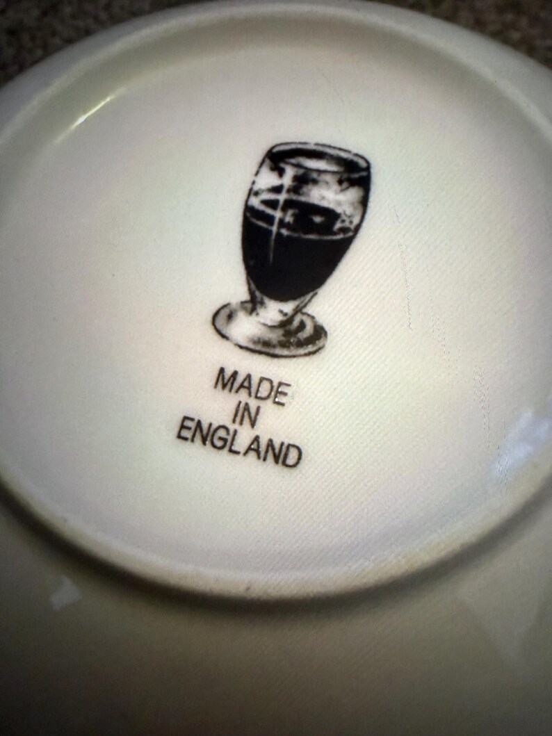 May include: A white ceramic plate with a black illustration of a glass of dark liquid. The words "MADE IN ENGLAND" are printed below the illustration.