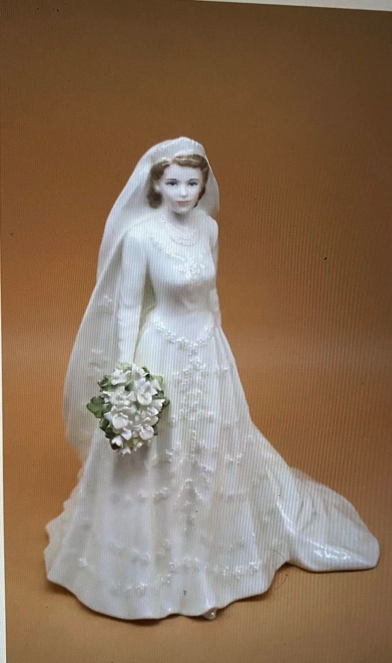 May include: A porcelain figurine of a bride wearing a white gown with a long veil and holding a bouquet of white flowers.