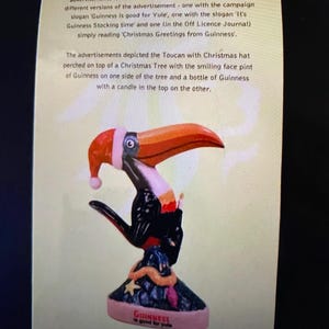 May include: A vintage Christmas advertisement for Guinness Stout featuring a toucan wearing a Santa hat perched on a Christmas tree. The toucan is holding a pint of Guinness and a bottle of Guinness with a candle on top. The text reads "Guinness is good for Yule".