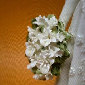 May include: A white porcelain figurine of a bride holding a bouquet of white flowers with green leaves.