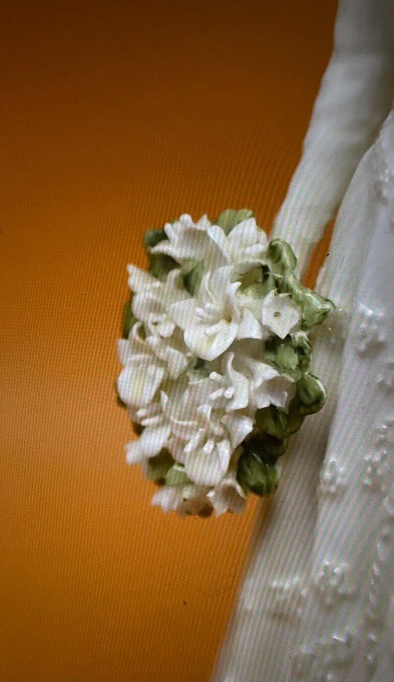 May include: A white porcelain figurine of a bride holding a bouquet of white flowers with green leaves.