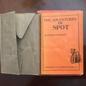 Könnte beinhalten: Die Abenteuer von Spot von Rodney Bennett, ein Kinderbuch mit orangefarbenem Einband und einer Schwarzweißillustration eines Hundes auf der Vorderseite.