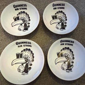 May include: Four white ceramic bowls with a black and white Guinness toucan design. Each bowl has the text "GUINNESS HIM STRONG" at the top. The toucan holds a rugby ball and two pints of Guinness.