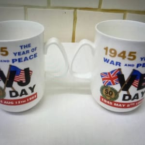Könnte beinhalten: Zwei weiße Keramikbecher mit einem Gedenkdesign zum 50. Jahrestag des VJ-Tages. Die Becher zeigen den Text "1945 The Year of War and Peace" und "VJ Day 1945 Aug 15th 1995" sowie "1945 The Year of War and Peace" und "VE Day 1945 May 8th 1995". Die Becher zeigen auch gekreuzte Flaggen der Vereinigten Staaten und des Vereinigten Königreichs.