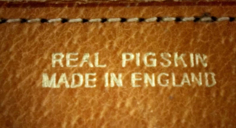 Puede incluir: Primer plano de una superficie de cuero marr&oacute;n con el texto "REAL PIGSKIN MADE IN ENGLAND" en relieve en blanco.