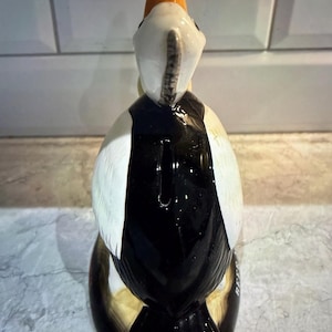 May include: A ceramic puffin figurine with a black and white body, white wings, and an orange beak. The bird is standing upright, with a glossy finish. The figurine is a decorative item.