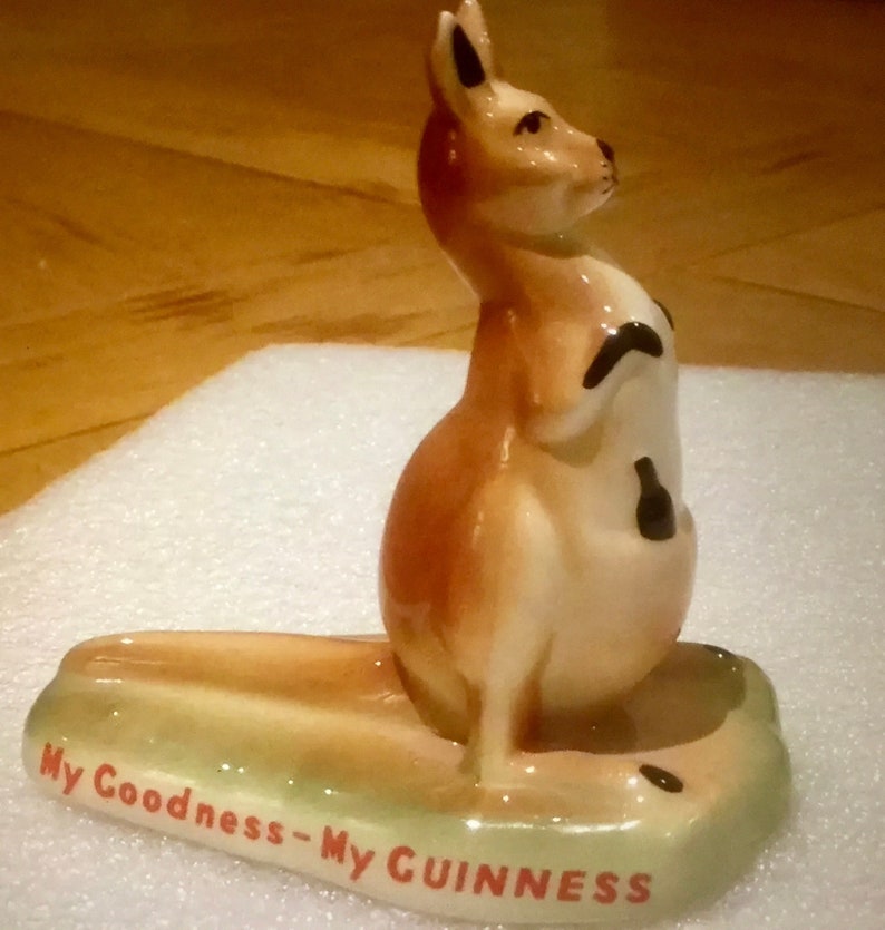 K&ouml;nnte beinhalten: Keramik-K&auml;nguru-Figur in Beige-, Braun- und Cremet&ouml;nen, mit einem kleinen schwarzen Flaschendetail. Der Sockel ist gr&uuml;n mit dem Text "My Goodness - My GUINNESS" in Rot.