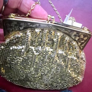 Puede incluir: Un bolso de noche de malla dorada con una correa de cadena y un diseño floral en el cierre.