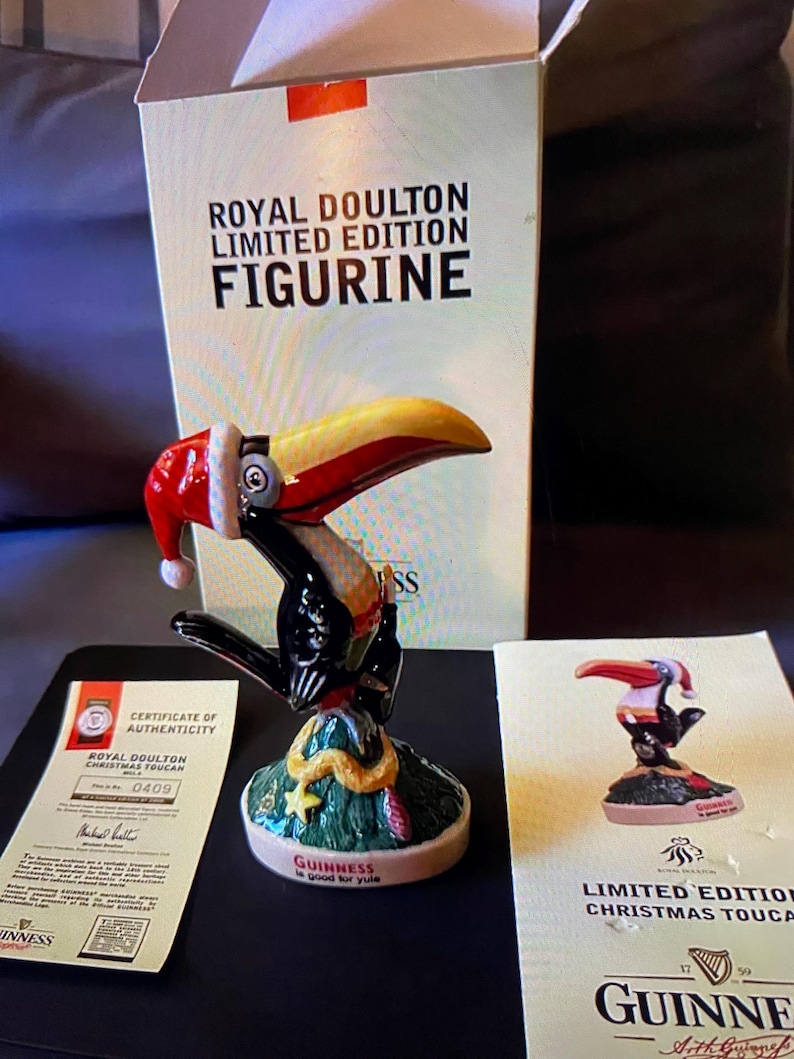 May include: A Royal Doulton limited edition Christmas toucan figurine. The toucan is wearing a Santa hat and is perched on a green tree with a snake. The base of the figurine reads "Guinness is good for Yule".