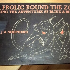 May include: A black book cover with a white illustration of a monkey and a cat laughing. The title of the book is "A Frolic Round The Zoo" and the subtitle is "Being The Adventures Of Blinx & Bunda". The author is "J.A. Shepherd".