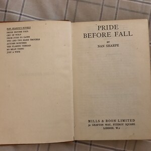 May include: A book titled "Pride Before Fall" by Nan Sharpe. The book is a paperback and has a white cover with black text. The book is part of a series of novels by Nan Sharpe, which are listed on the front cover.