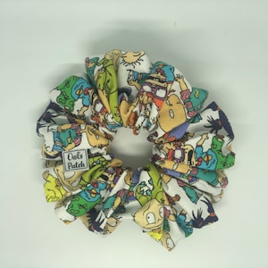 May include: A white scrunchie with a colorful cartoon print of characters from the Nickelodeon show "Rugrats". The scrunchie has a small label that says "Owls Patch".