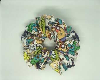 May include: A white scrunchie with a colourful cartoon print of characters from the Nickelodeon show "Rugrats". The scrunchie has a small label that says "Owls Patch".