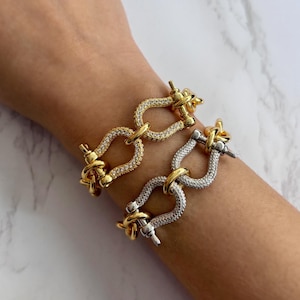 May include: Two gold and silver bracelets with a chain link design and a clasp closure. The bracelets are adorned with small, clear rhinestones.